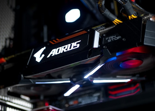 A close-up view of a high-performance graphics card inside a computer, featuring prominent branding and illuminated components. The cables and surrounding hardware components are partially visible, contributing to a sleek, modern tech aesthetic.