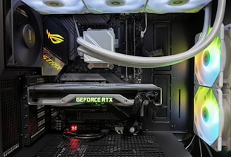 Inside view of a computer case showcasing a sophisticated gaming setup. Visible components include a GeForce RTX graphics card illuminated with green lighting, an ASUS motherboard, cooling fans with LED lighting, and a liquid cooling system with white tubes. Cables are neatly organized, and overall, the hardware suggests a high-performance machine.