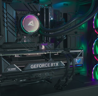 The image depicts the inside of a computer case featuring a high-performance graphics card labeled 'GEFORCE RTX' with RGB lighting. The cooling fans are illuminated with vibrant colors, creating a visually striking look. Various cables and components are neatly arranged, highlighting advanced hardware and a focus on aesthetics.